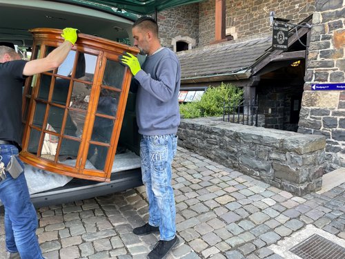 Die Museumstechniker der Burg Altena transportieren den Glasaufsatz eines Biedermeierschranks in die Räume der Sonderausstellung. Foto: Bernadette Lange