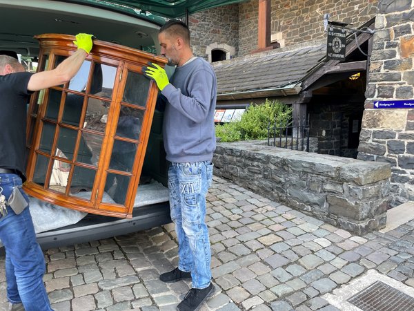 Die Museumstechniker der Burg Altena transportieren den Glasaufsatz eines Biedermeierschranks in die Räume der Sonderausstellung. Foto: Bernadette Lange