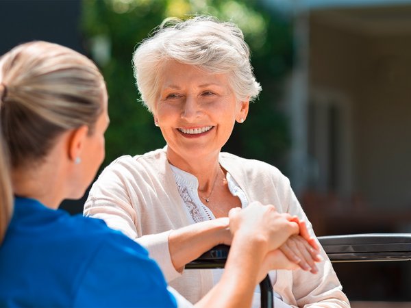 Zu sehen ist eine weibliche Pflegekraft mit einer alten Dame im Gespräch