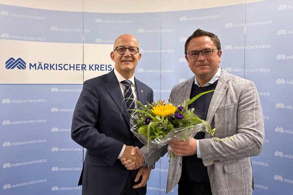 Der amtierende Landrat Marco Voge (rechts im Bild) überreicht dem zukünftigen Landrat Ralf Schwarzkopf einen Blumenstrauß. Foto: Alexander Bange / Märkischer Kreis